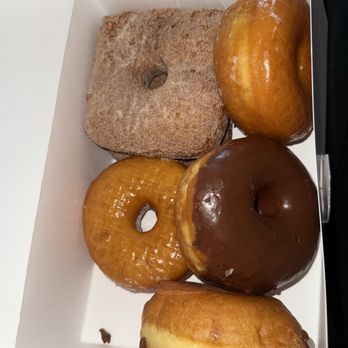 A white box with a cinnamon sugar square, a glazed raised, a chocolate frosted and a glazed donut