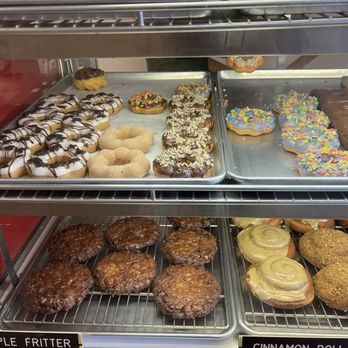Display case shelves lined with trays of apple fritters and cinnamon rolls